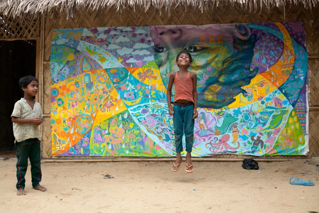 A child is jumping happily in front of a graffiti wall, another boy watches on